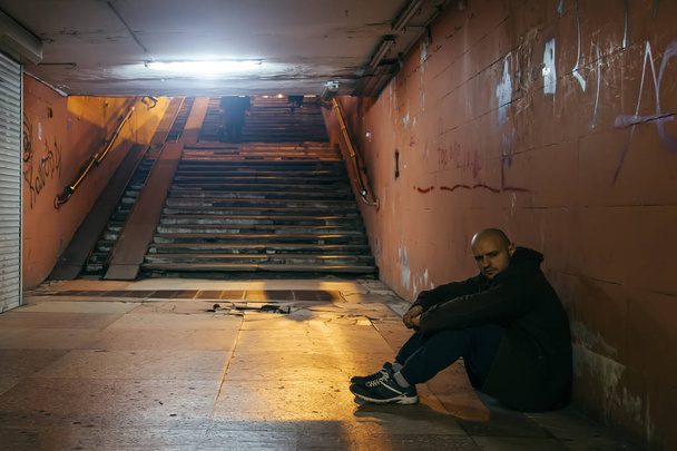 悲しい男が地下鉄のトンネルの地面に座っている. - 写真・画像