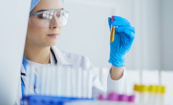 Eine medizinische oder wissenschaftliche Forscherin oder Ärztin betrachtet ein Reagenzglas mit klarer Lösung in einem Labor - Foto, Bild