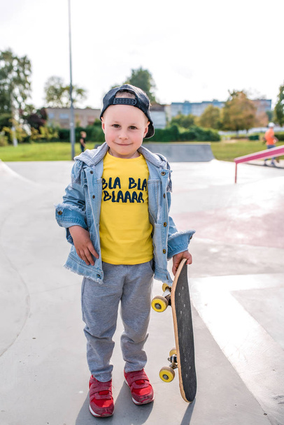 little boy of 3-5 years old laughs, plays, relaxes, on summer autumn day in city park, fun casual clothes, skateboard board in his hand, casual clothes. - Foto, Imagem