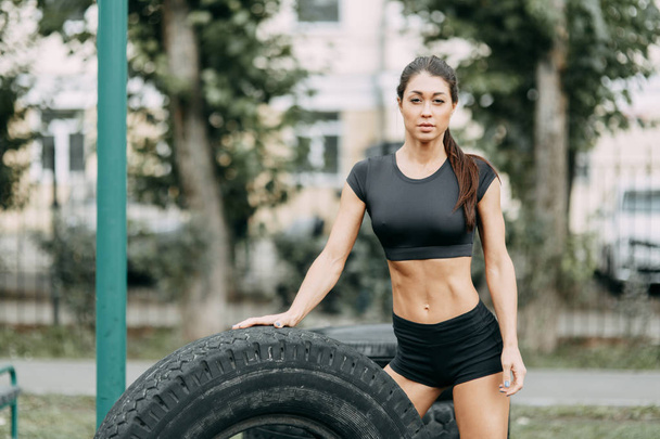 Training and posing with a tire. Beautiful athletic girl on the Playground.  - Foto, afbeelding