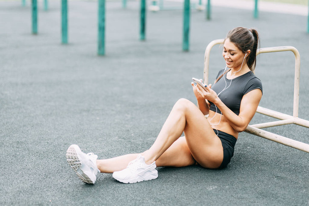 Music, rest and relaxation with phone and headphones. Beautiful athletic girl on the Playground.  - Photo, image