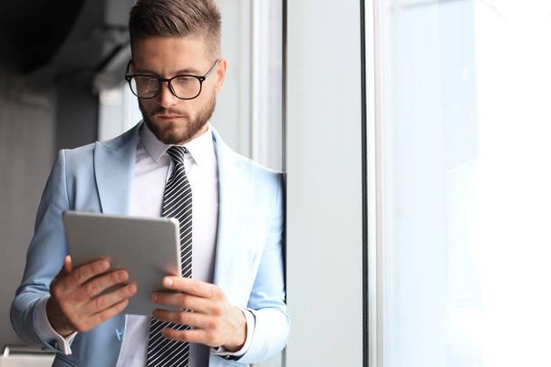Modern business man in formalwear using digital tablet while standing near window in the office - Фото, зображення