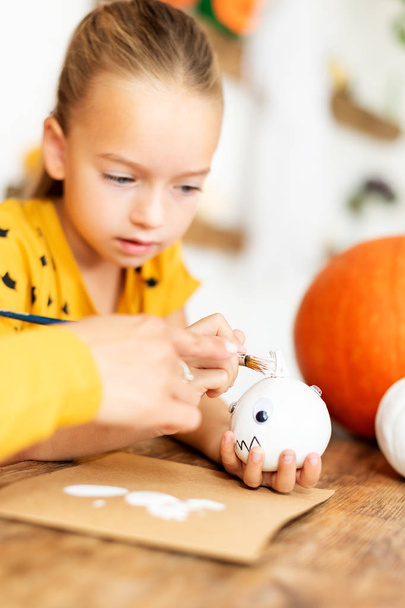 Roztomilá mladá dívka, která sedí u stolu a maluje s matkou malé bílé dýně. DIY Halloween svátek a rodinný život. - Fotografie, Obrázek