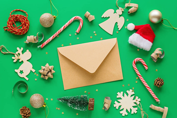Christmas composition. Craft paper envelope and toys on green background. new year concept. Greeting card, winter holidays, xmas celebration 2020. Flat lay, top view, copy space, mockup, template - Foto, Imagen