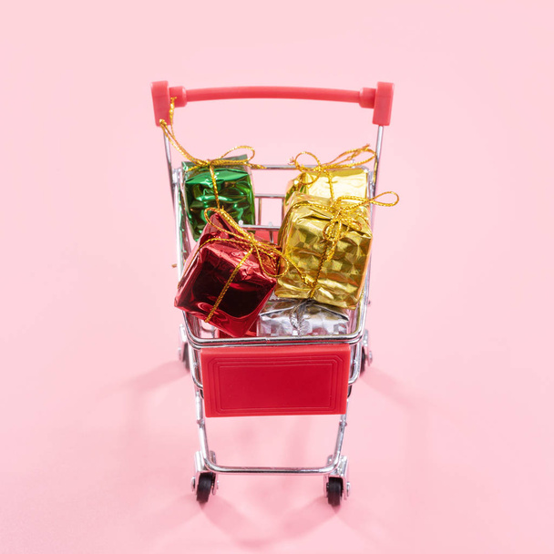 Jahresverkauf, Weihnachts-Shopping-Saison-Konzept - Mini-roter Einkaufswagen voller Geschenkschachteln isoliert auf blassrosa Hintergrund, Kopierraum, Nahaufnahme - Foto, Bild