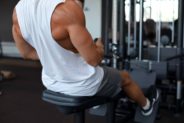 Fit and muscular man using rowing machine at gym. Back view - Photo, Image