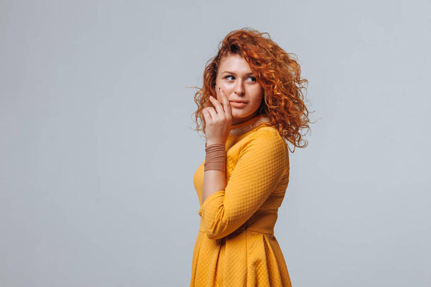 A red haired girl in a yellow dress on a light gray background s - Foto, imagen