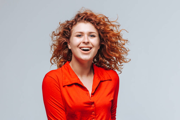 Egy vörös hajú mosolygós lány portréja szürke háttérrel - Fotó, kép