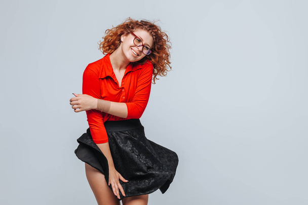 Curly redhead girl in red skirt and glasses smiling - 写真・画像