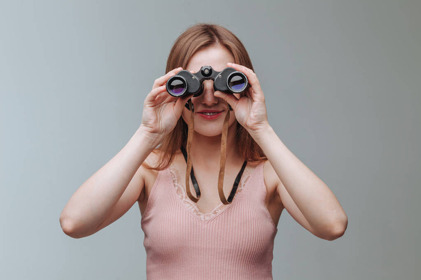 Girl looking through binoculars on a gray background - Foto, imagen