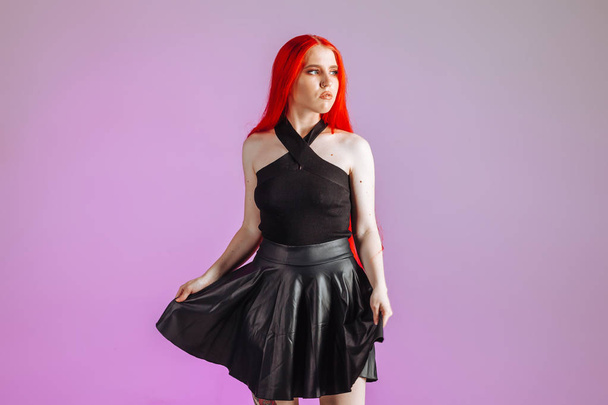 Girl with red long hair and leather skirt posing on pink backgro - Foto, Imagen