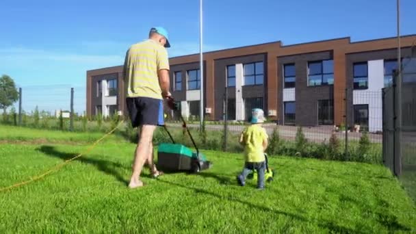 Divertidos chicos papá e hijo cortando hierba en el patio del apartamento privado. Movimiento del cardán
 - Imágenes, Vídeo