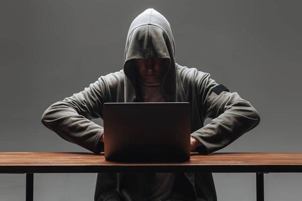 Hacker in a hood without a face sitting at a laptop - Fotoğraf, Görsel