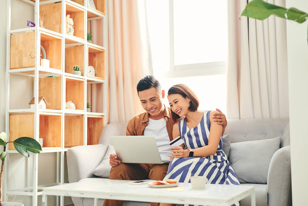 Jovem casal asiático de compradores comprando on-line com cartão de crédito e um laptop em casa
  - Foto, Imagem