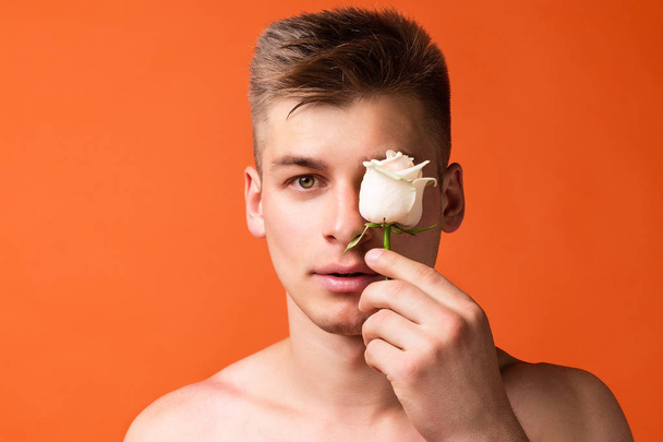 Ένας άντρας κρατά ένα λουλούδι, κλείνοντας τα μάτια του με αυτό.. - Φωτογραφία, εικόνα