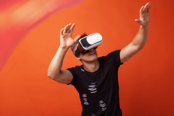 Młody człowiek w wirtualnej rzeczywistości z zestawem słuchawkowym na głowie w pomarańczowym studiu w tle - Zdjęcie, obraz