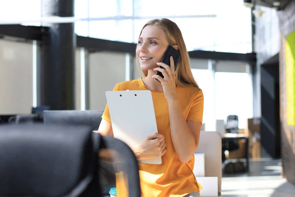Attractive business woman talking with collegues on the mobile phone while sitting on the office desk - Foto, Imagen
