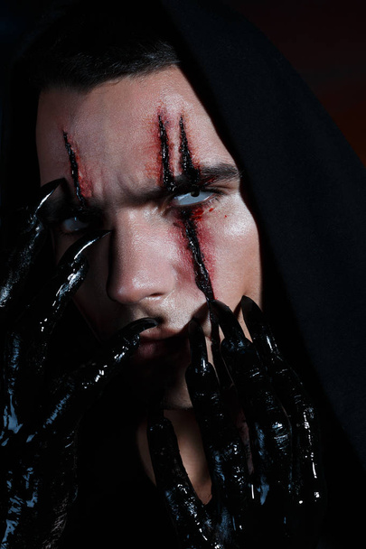 Musta taikuri raapii kasvojaan mustilla kynsillä jättäen siihen verisiä jälkiä. Halloween kauhu käsite
 - Valokuva, kuva