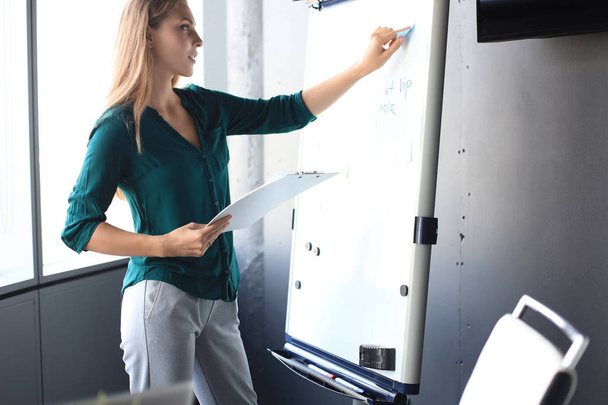 Beautiful business woman is standing near flipchart and examining information at it - Photo, Image