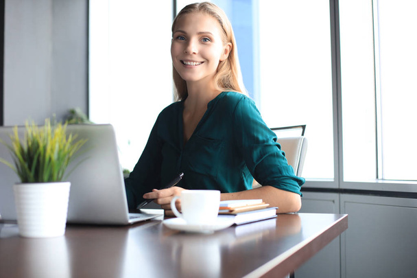 Beautiful smiling business woman is sitting in the office and looking at camera - Foto, Imagen