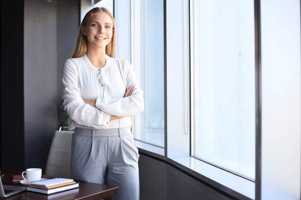 Attractive business woman looking at camera and smiling while standing in the office - Foto, Imagem