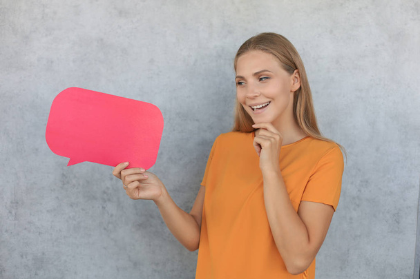 Happy beautiful young blonde woman standing isolated over gray background, holding empty speech bubble - Фото, изображение