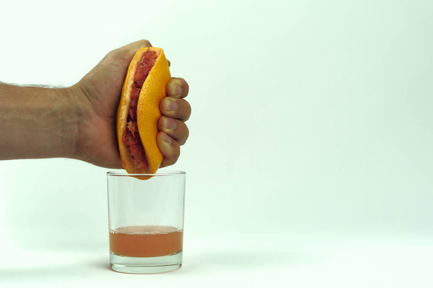 чоловік стискає половину соковитого грейпфрута до порожнього скла на білому фоні, крупним планом
 - Фото, зображення