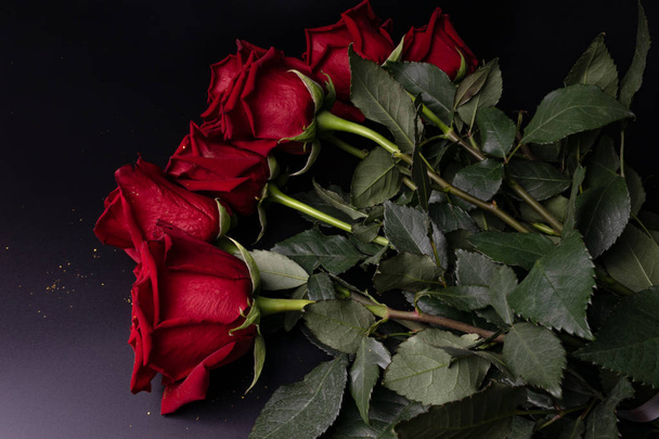 Rosas frescas de color rojo oscuro yacen sobre una mesa en una habitación oscura. Un regalo para un ser querido
 - Foto, Imagen