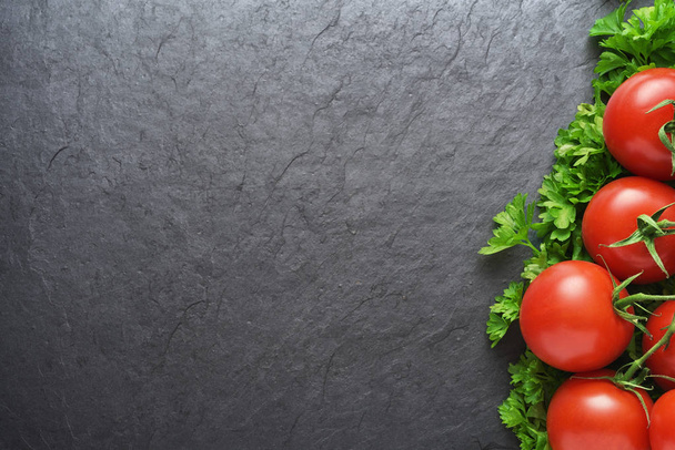 Czerwone pomidory i pietruszka na czarnym łupku z kopią przestrzeni - Zdjęcie, obraz