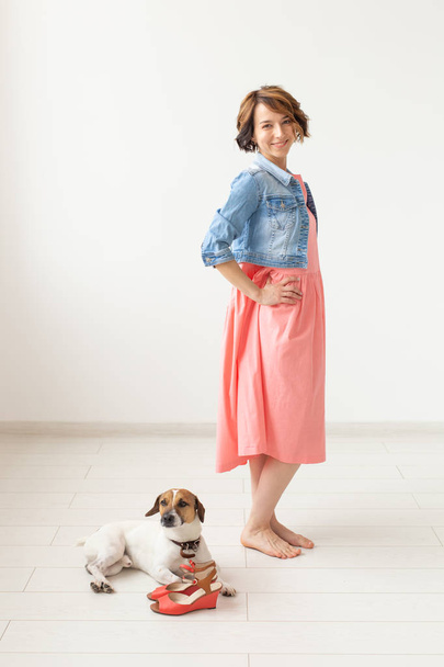 Young cheerful woman in a long dress and denim dress with her beloved dog posing on a white background. The concept of daily clothing. - Photo, Image