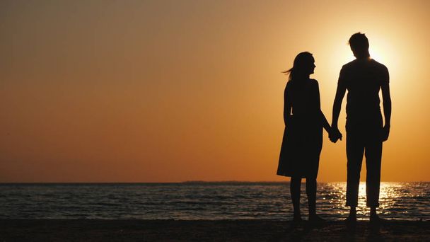 Silhouettes d'un jeune couple amoureux debout près de la mer au coucher du soleil
 - Photo, image