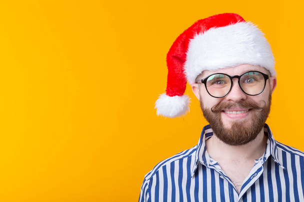 Gioioso pazzo carino giovane hipster maschio in rosso cappello di Babbo Natale posa su sfondo giallo. Il concetto di Natale e il nuovo anno. Spazio pubblicitario
. - Foto, immagini