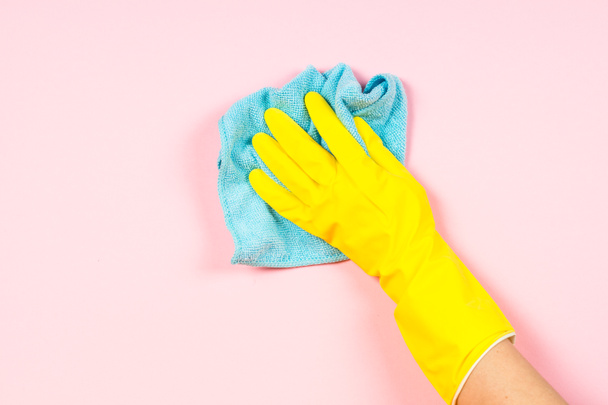 Hand in gele handschoenen en microfiber Rag reiniging roze achtergrond. - Foto, afbeelding