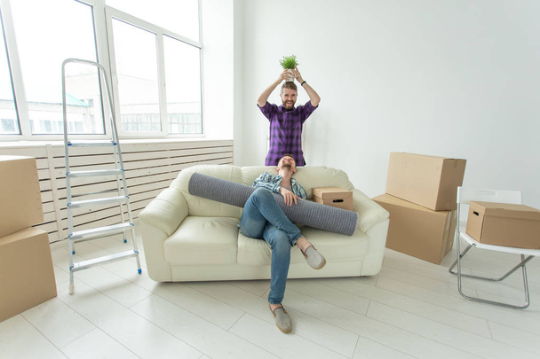 Twee student mannelijke vrienden houden hun spullen in hun handen zitten in de woonkamer van een nieuw appartement. Housewarming concept - Foto, afbeelding