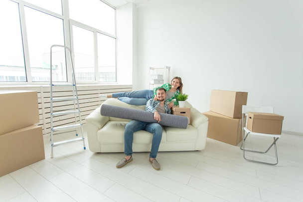 Χαρούμενο νεαρό ζευγάρι χαίρεται για τη μετακίνηση σε ένα νέο σπίτι που θέτει τα υπάρχοντά τους στο σαλόνι. Έννοια του σπιτιού και των ενυπόθηκων δανείων για μια νεαρή οικογένεια - Φωτογραφία, εικόνα