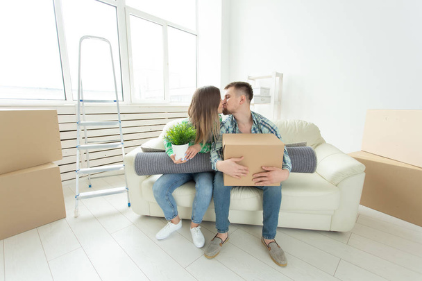 Přesun a nemovitostí koncept - šťastný pár líbání na pohovce v jejich novém bytě - Fotografie, Obrázek