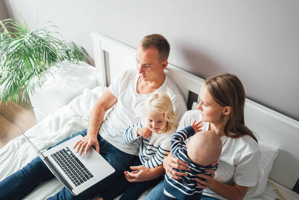 Młoda matka opiekuje się dzieckiem, podczas gdy ojciec pracuje na laptopie. Rodzina w domu - Zdjęcie, obraz