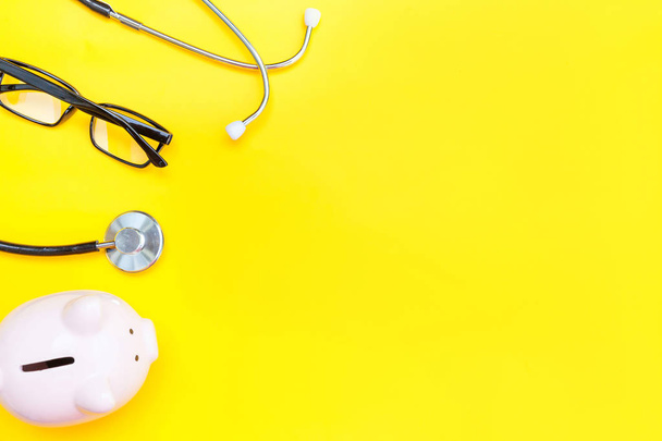 Equipamento médico medicina estetoscópio ou fonendoscópio óculos de banco piggy isolado no fundo amarelo na moda
 - Foto, Imagem