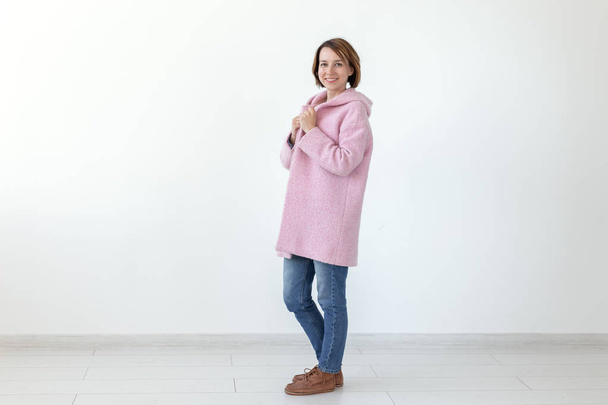 Charming young female model posing on a white background in a designer pink coat. The concept of a unique handicraft design. Advertising space, copyspace - Fotó, kép