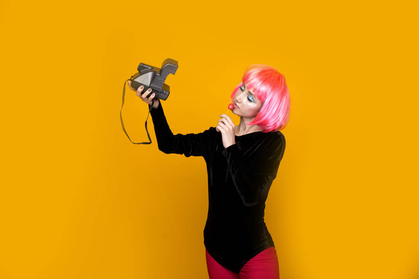 90s fashion concept. Girl in a pink wig holding camera. - Фото, изображение