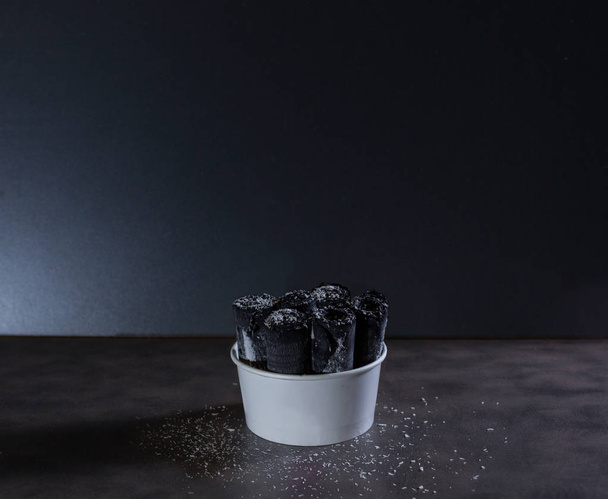 Délicieuse glace noire thaïlandaise roulée sur table noire avec fond sombre et copeaux de noix de coco
 - Photo, image