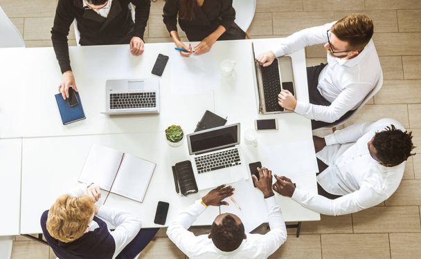 A team of young businessmen sitting at the table, top view, working and communicating together in an office. Corporate businessteam and manager in a meeting. - Φωτογραφία, εικόνα