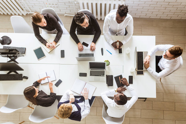 Μια ομάδα νέων επιχειρηματιών που κάθονται στο τραπέζι, βλέπουν από ψηλά, εργάζονται και επικοινωνούν μαζί σε ένα γραφείο. Εταιρικός ατμός και διαχειριστής σε συνάντηση. - Φωτογραφία, εικόνα