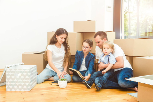 Glückliche junge Familie, Eltern Tochter und Sohn, packen Kisten aus und ziehen in ein neues Zuhause. Lustige Kinder rennen mit Kisten herein - Foto, Bild