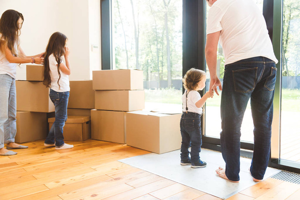 Щаслива молода сім'я, батьки дочка і син, розпаковують коробки і переїжджають в новий будинок. смішні діти бігають з коробками
 - Фото, зображення