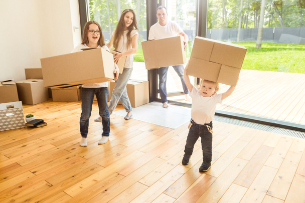 Щаслива молода сім'я, батьки дочка і син, розпаковують коробки і переїжджають в новий будинок. смішні діти бігають з коробками
 - Фото, зображення