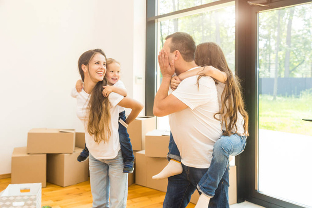 Happy young family, parents daughter and son, unpacking boxes and moving into a new home. funny kids run in with boxes - Foto, Imagem