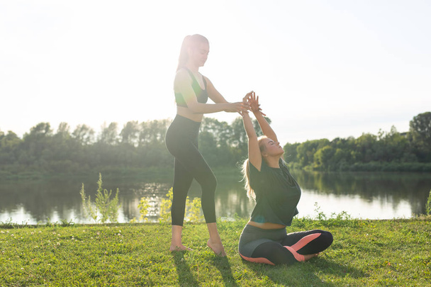Healthy lifestyle and people concept - Flexible women doing yoga in the summer park - Photo, Image