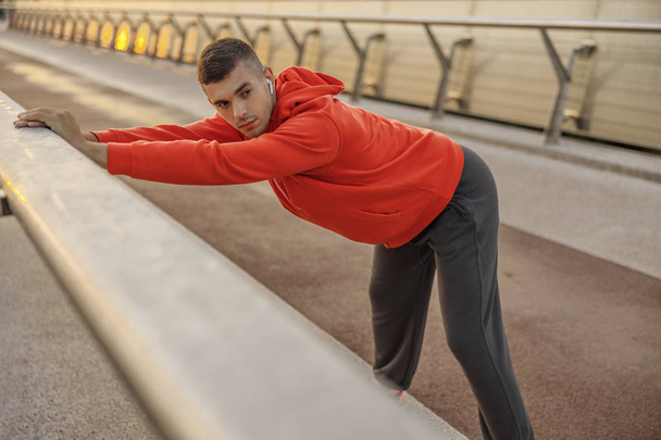 Sportive man with wireless earphones stretching outdoors - Photo, image