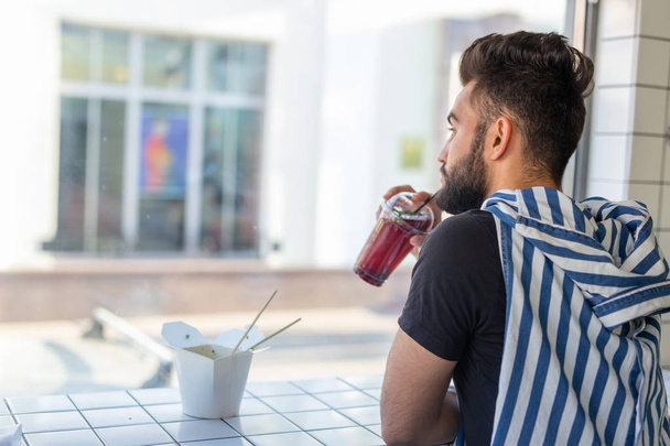 Bello giovane hipster ragazzo bere cocktail in un caffè e guardando nella finestra
. - Foto, immagini